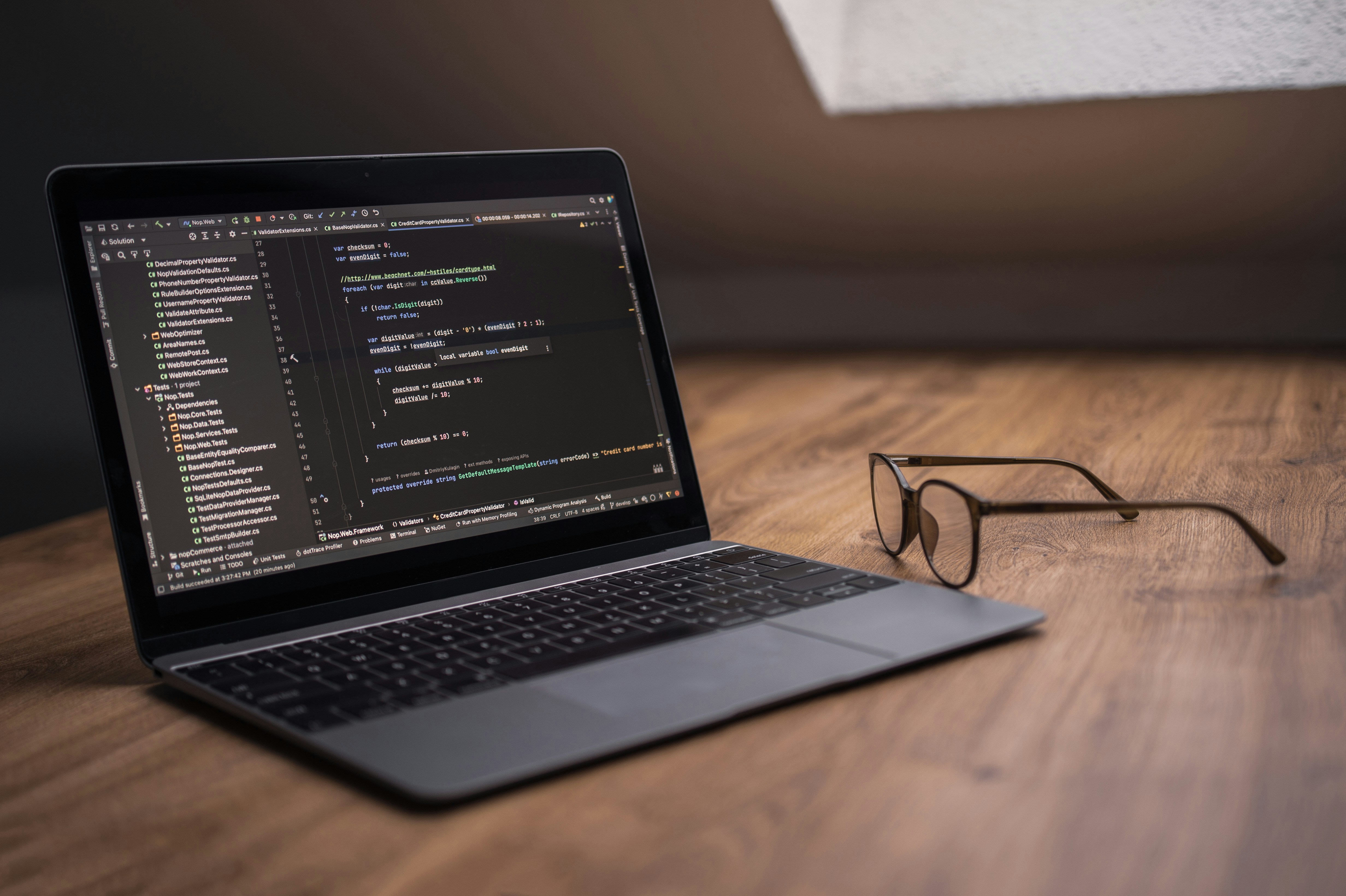 Laptop mit Code-Editor und Brille auf Holztisch
